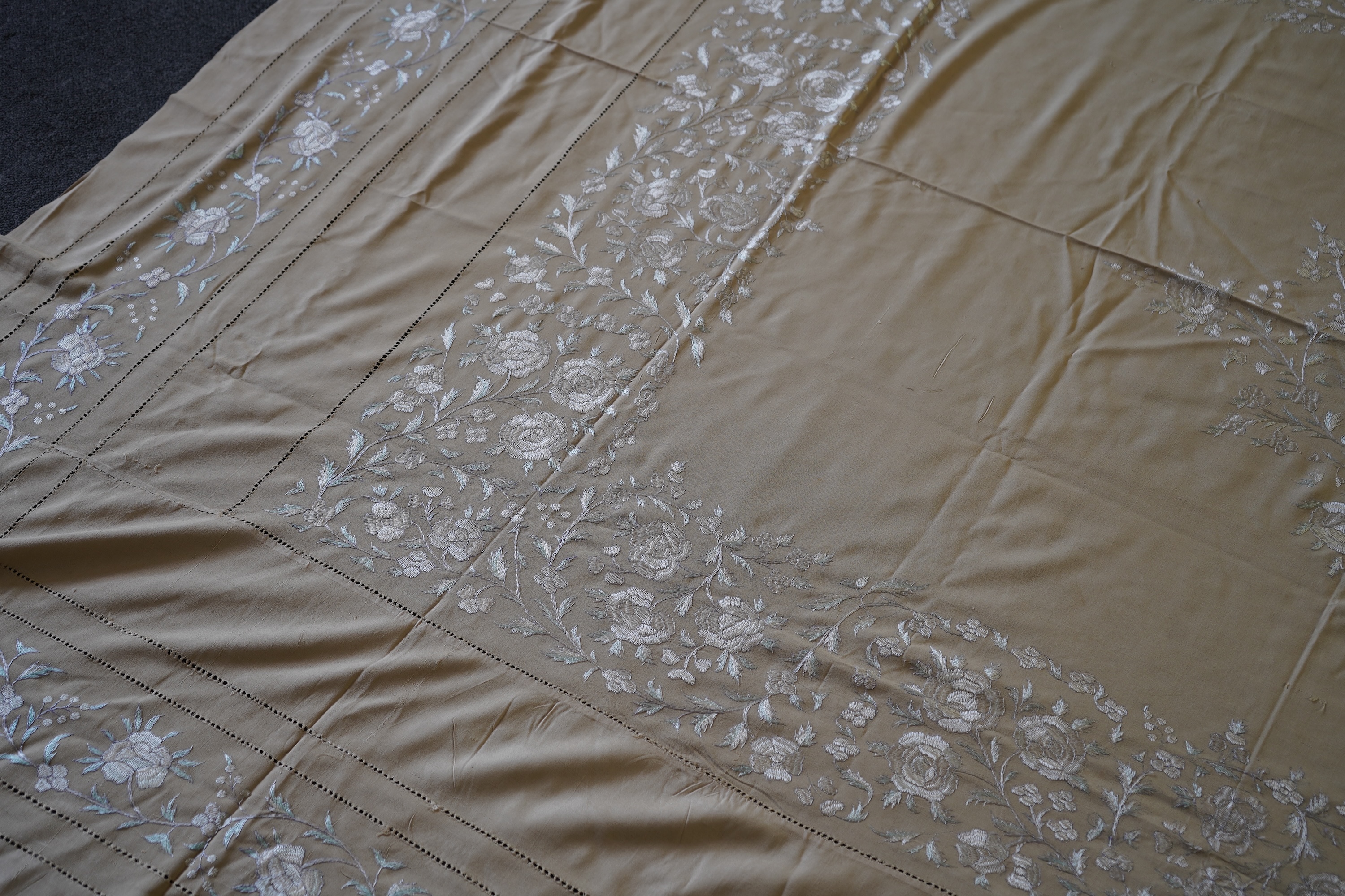 A 1920’s heavy shantung silk hand embroidered table cover. Worked with decorative rows of button hole stitch. Embroidered with white, green and blue silk flowers. 240cm x 204cm. Condition - some fine holes near corners,